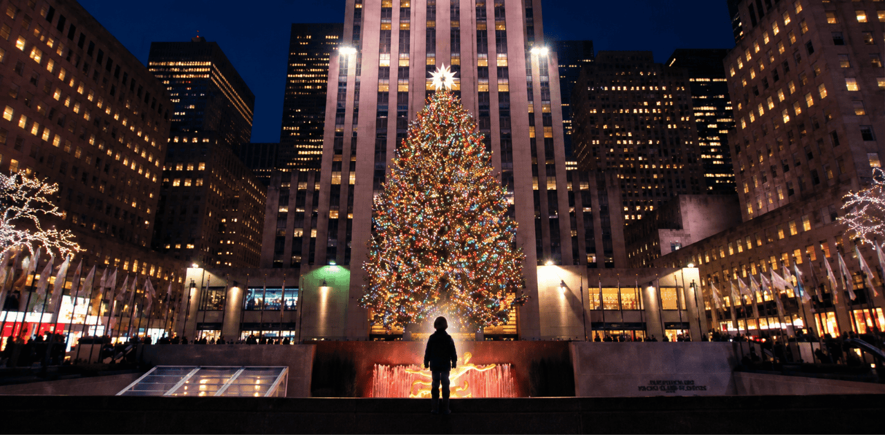 夜のニューヨークの広場に立つ少年と、ライトアップされた巨大なクリスマスツリー