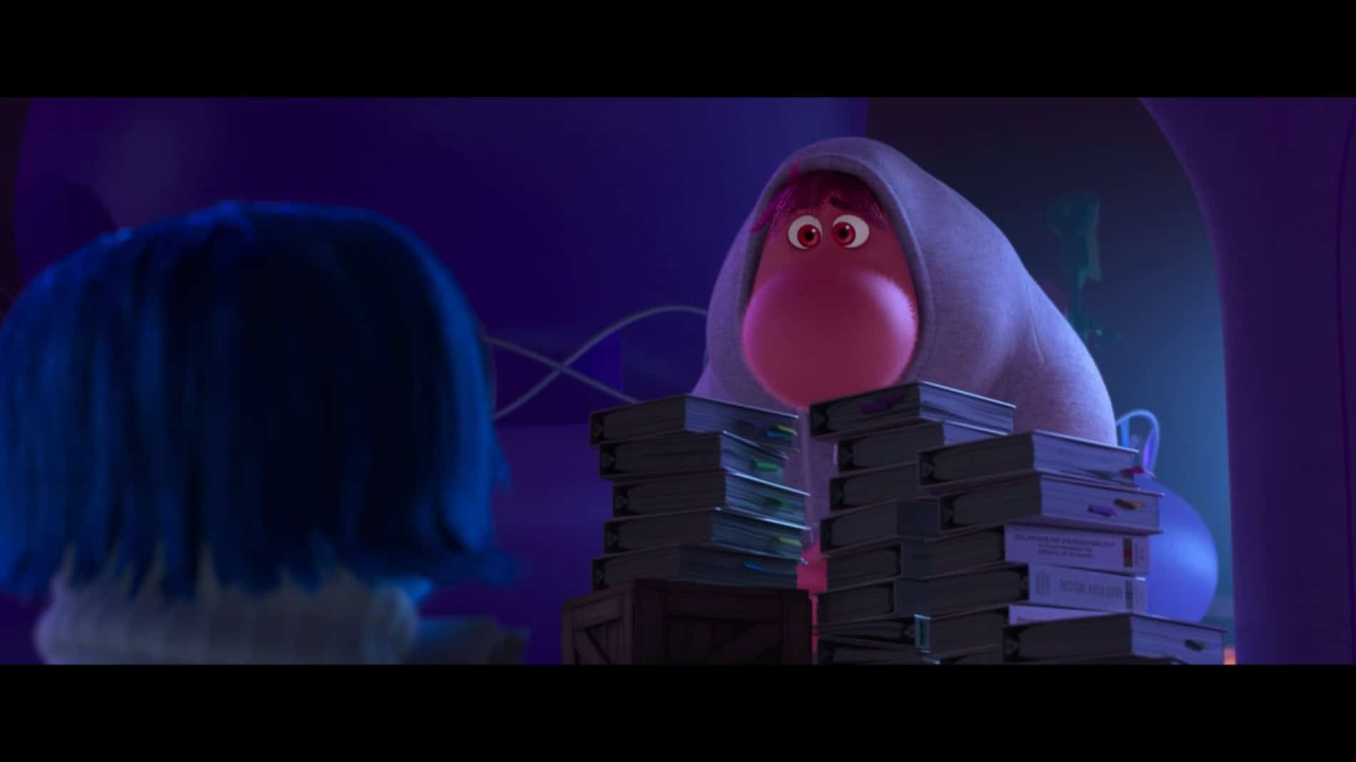 Embarrassment peeks out from behind a stack of books, with Sadness seen from behind in the foreground.